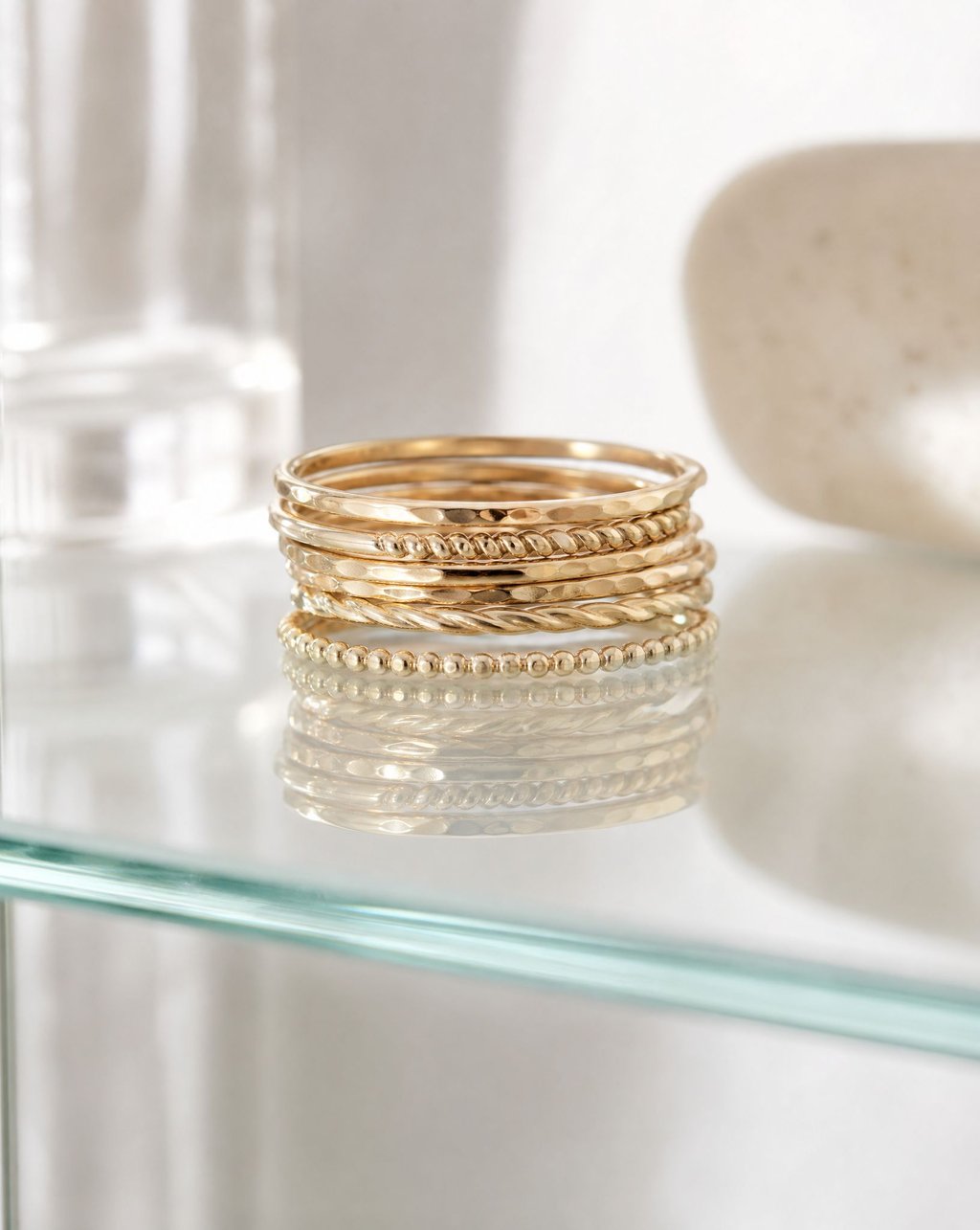 A stack of thin gold rings on a glass shelf with a reflection below