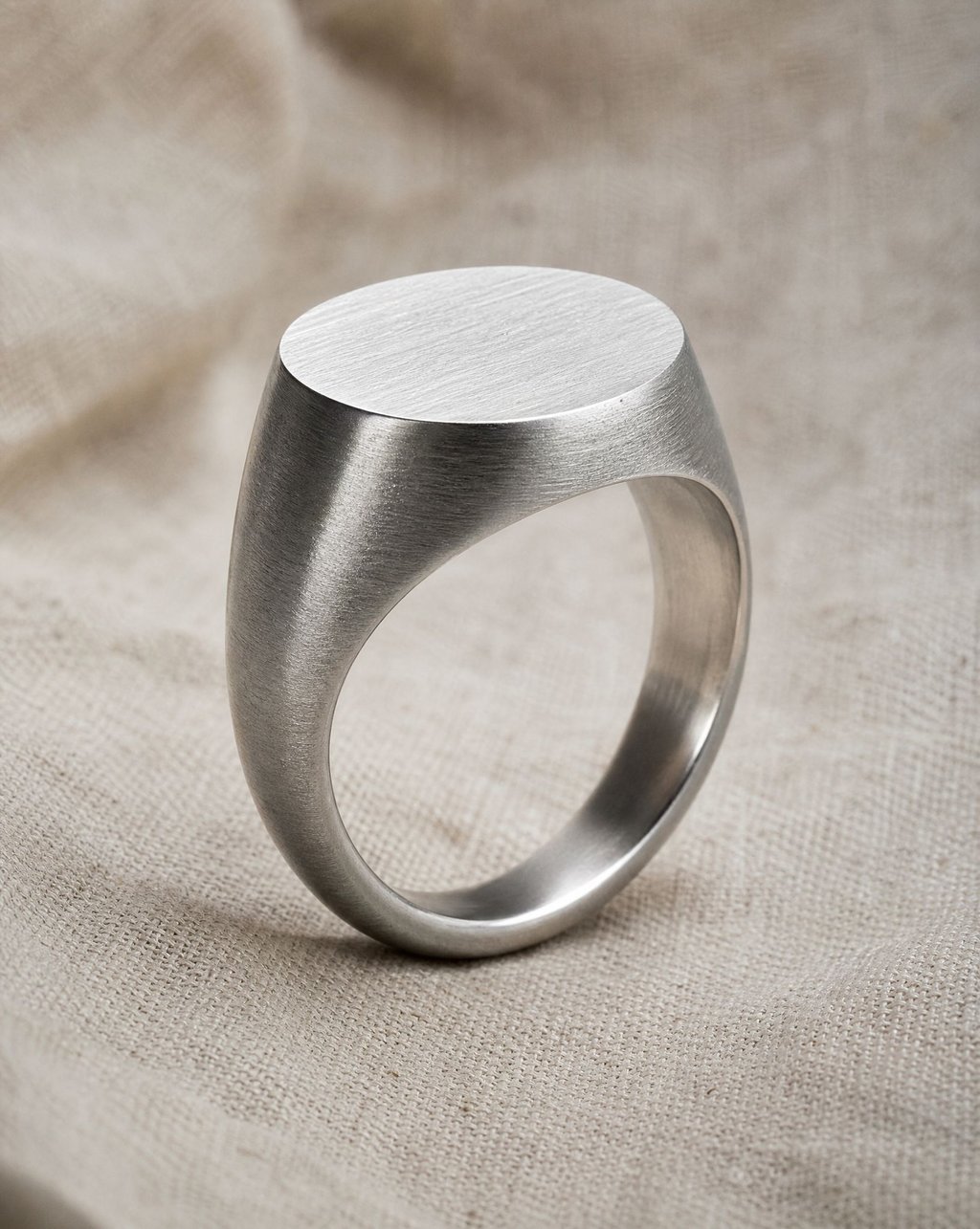 A brushed silver signet ring standing upright on linen fabric