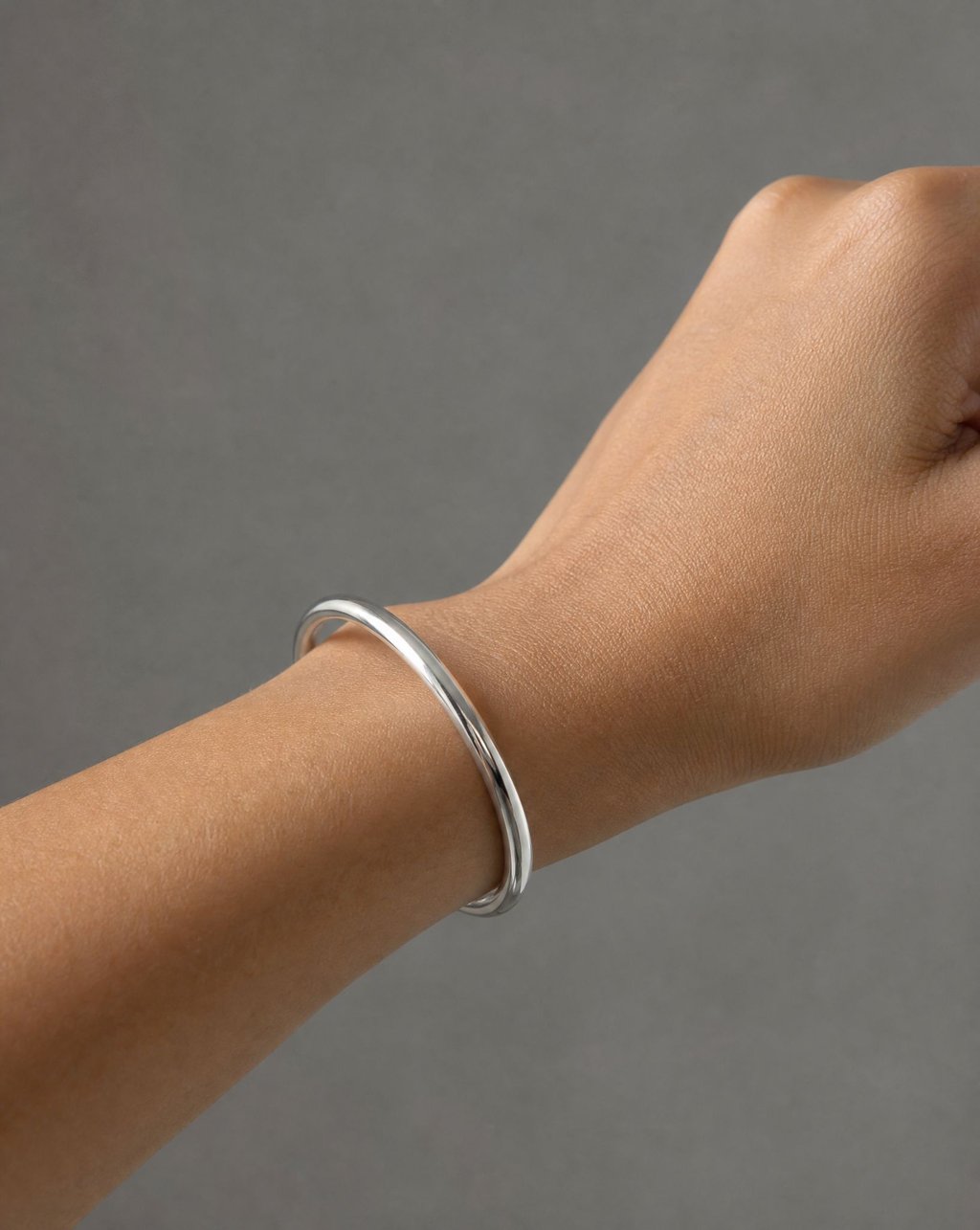 A polished silver bangle worn on a wrist against a grey backdrop