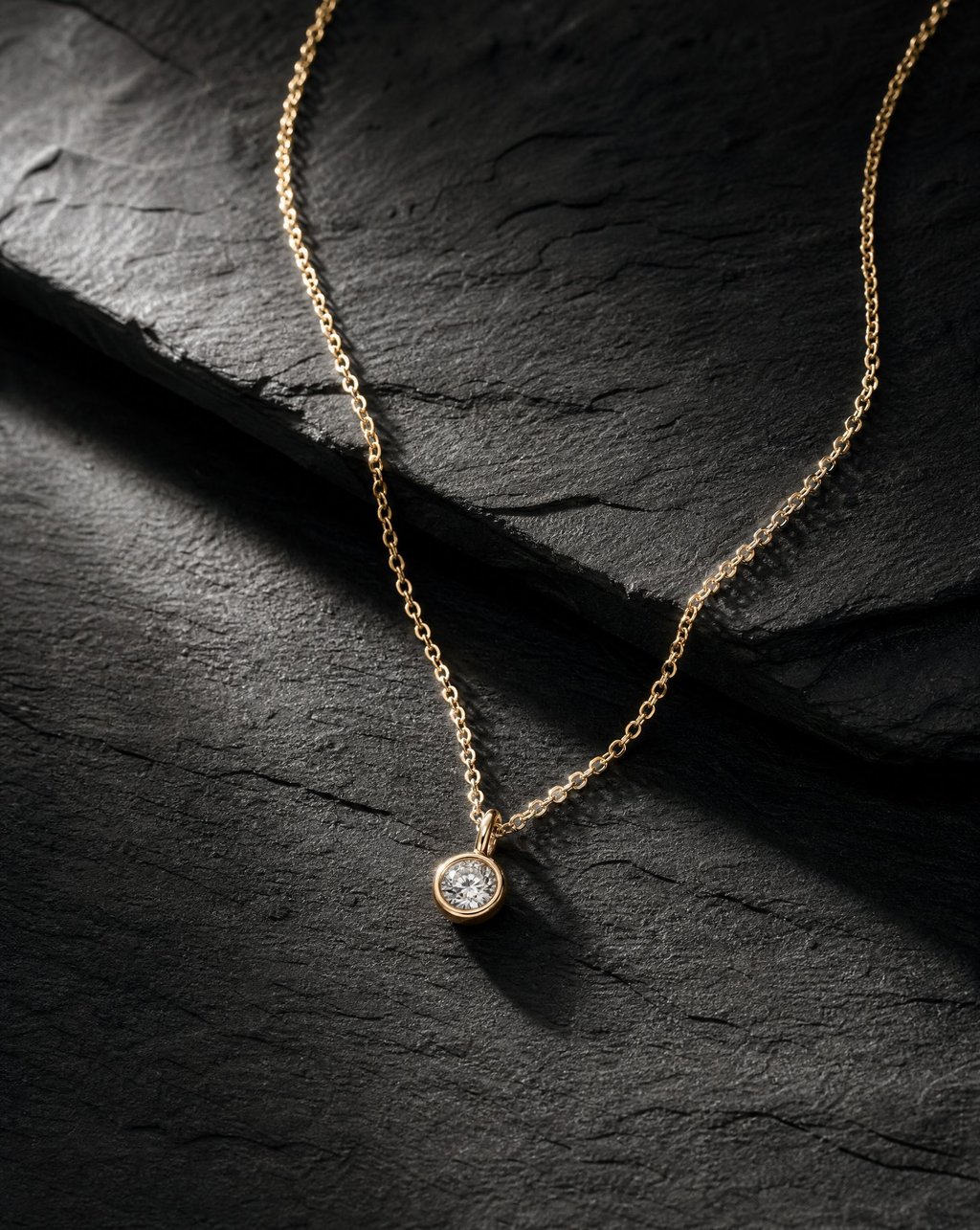 A fine gold chain necklace with a small round pendant on dark slate