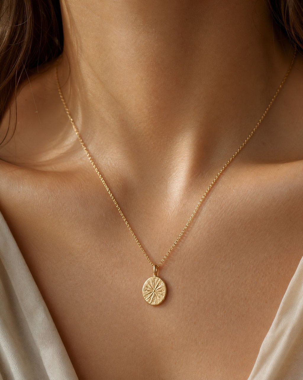 A fine gold pendant necklace worn at the collarbone in warm light