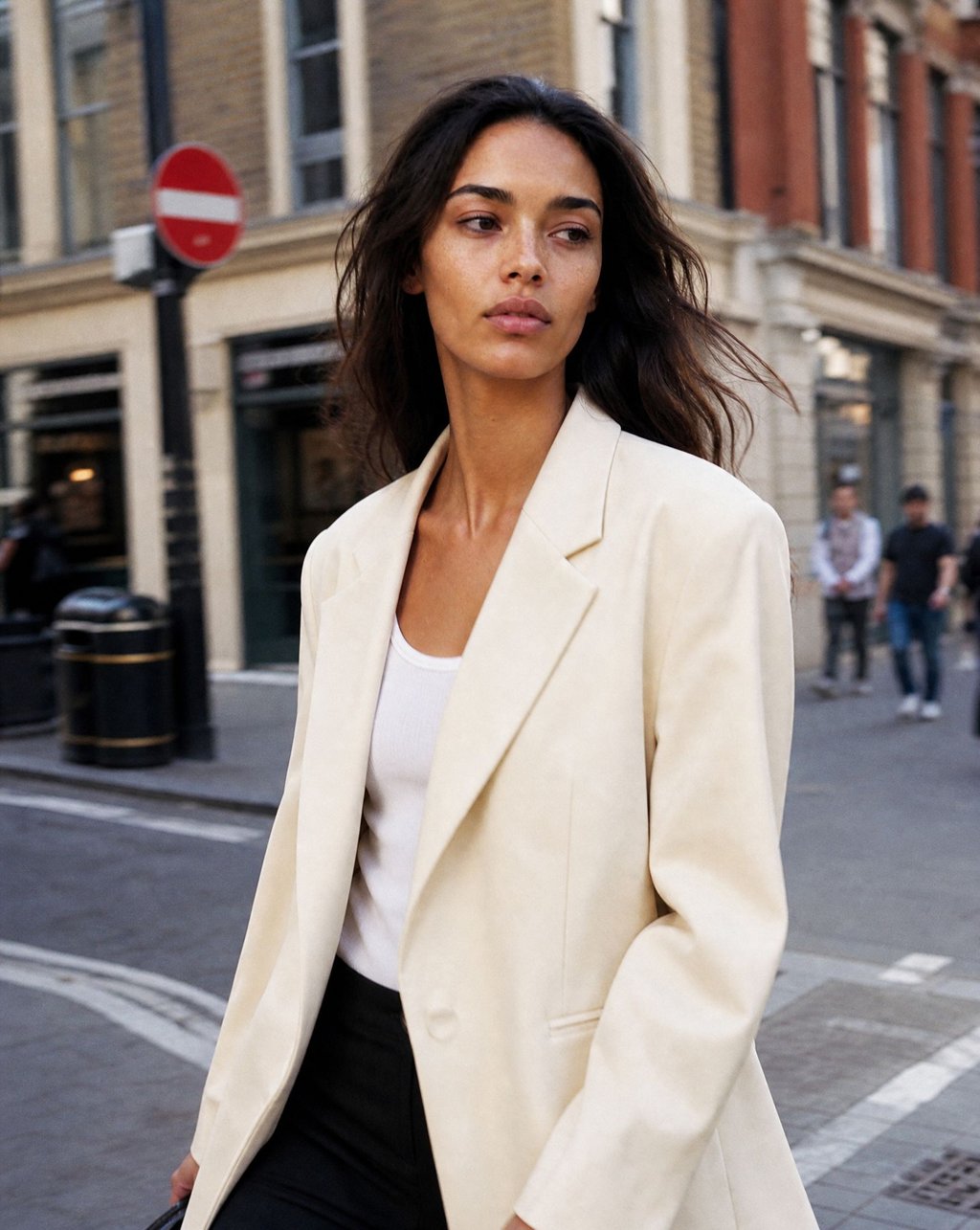 A woman in a cream blazer walking on a city street in daylight