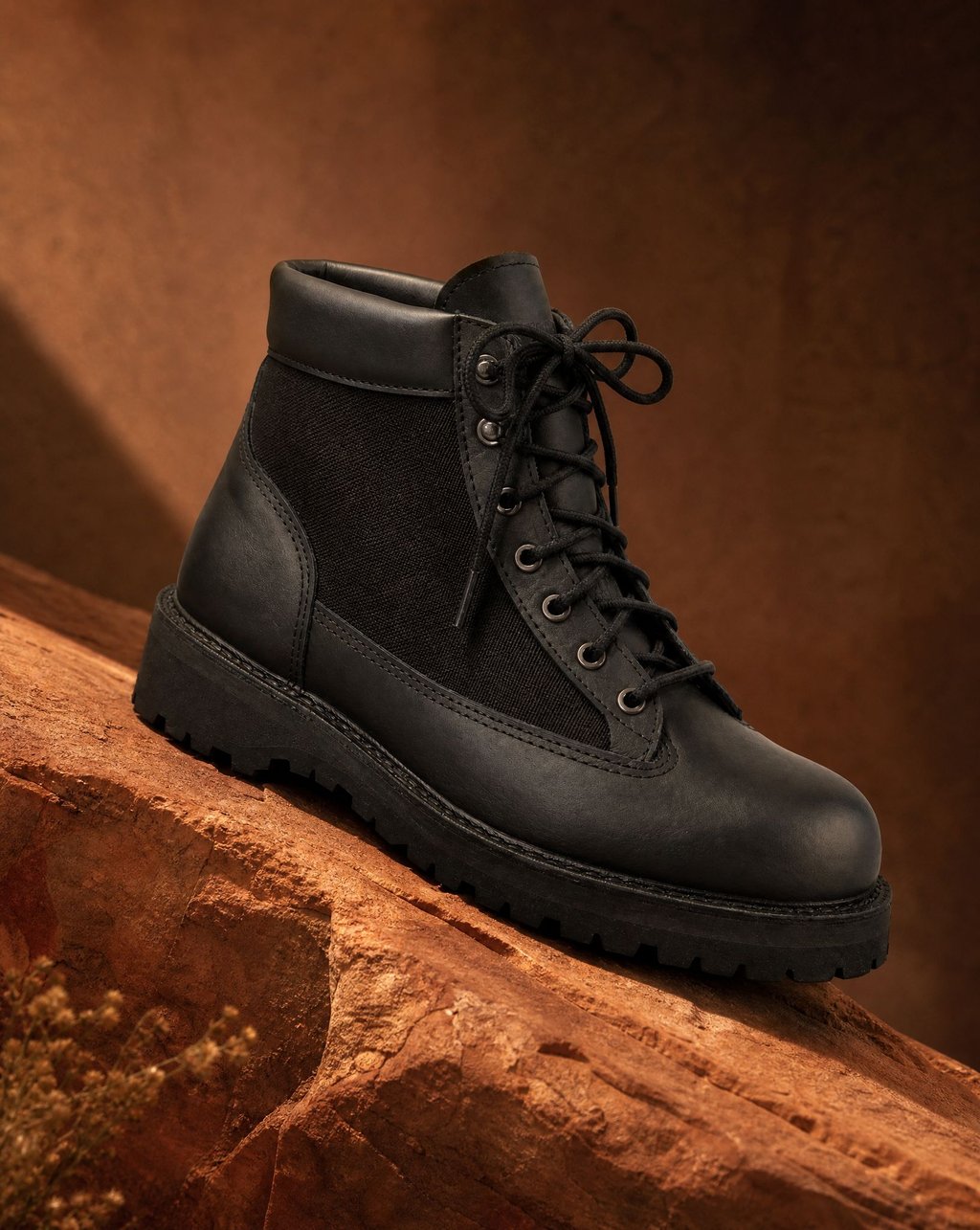 Black leather hiking boot on warm terracotta stone in soft raking daylight