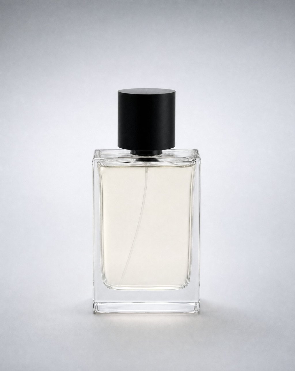A clear glass perfume bottle with a black cap on a soft grey-white gradient background under even light, the liquid level clearly visible