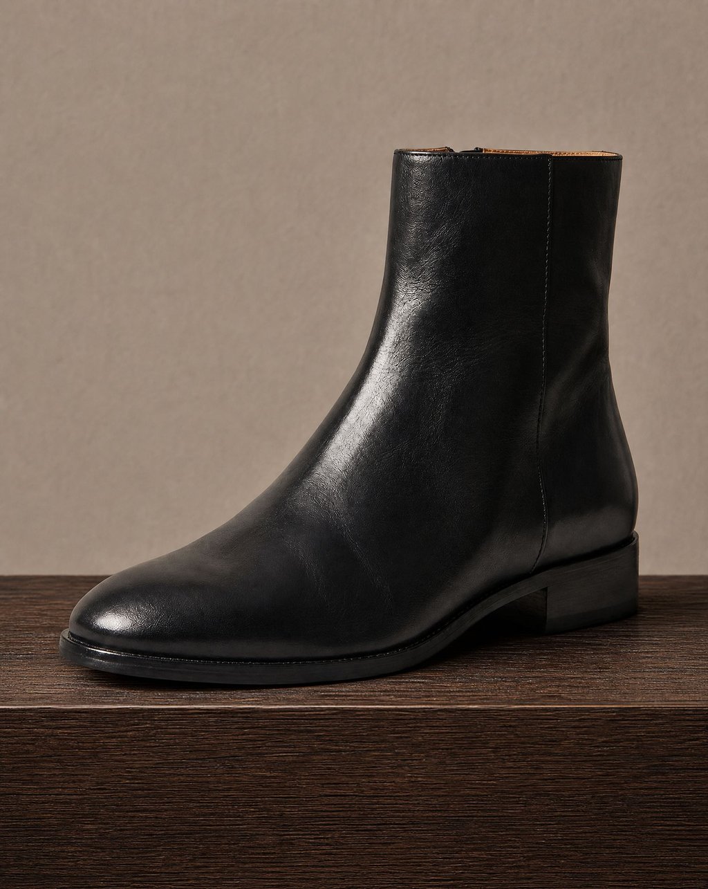 A single black leather ankle boot on a dark wood ledge, with the leather grain and the stitch line along the sole clearly resolved