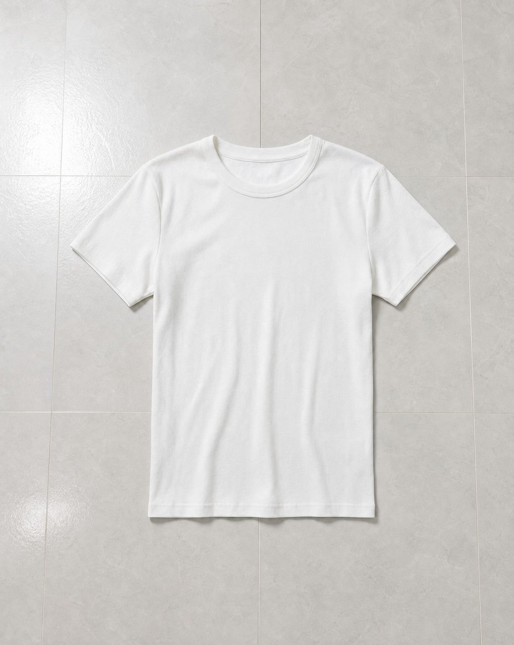 A white t-shirt laid flat on a pale grey tiled floor under even light