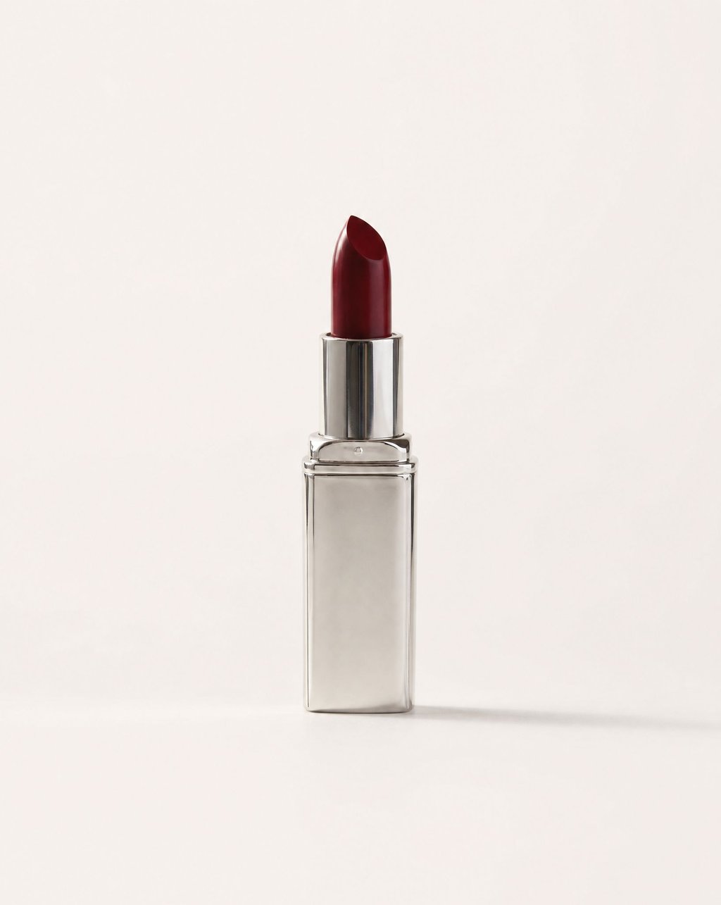 A red lipstick in a silver tube on a plain warm-white background under flat even light