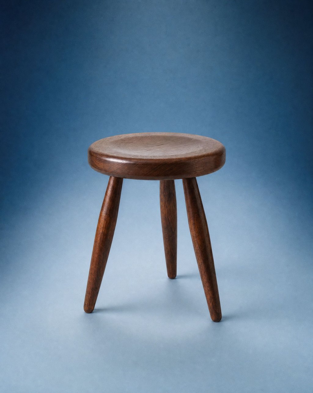 A small round wooden tripod stool on a clean seamless backdrop under soft centred light