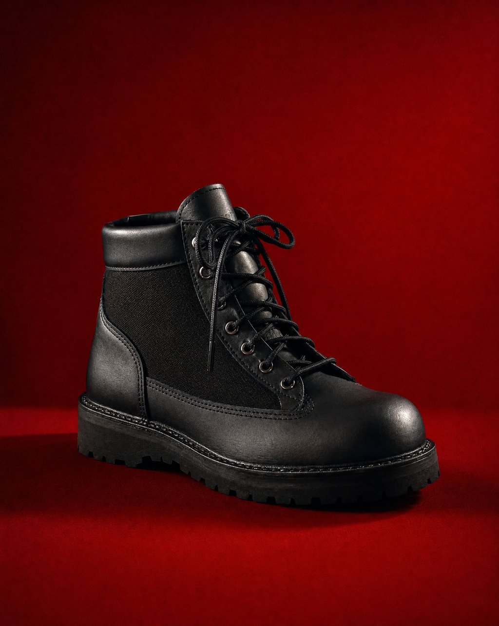 Black leather hiking boot against a deep sanguine red backdrop