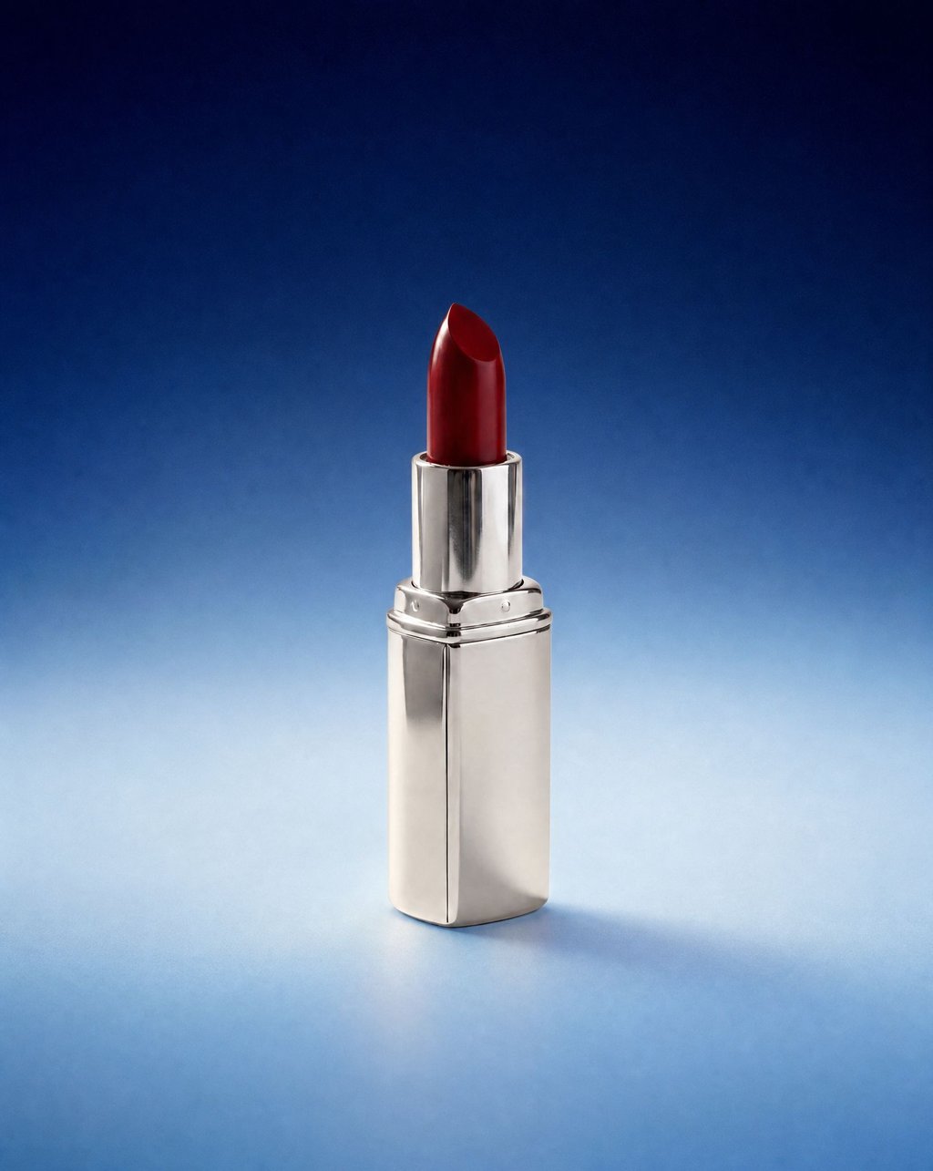A red lipstick in a polished silver tube standing on a blue gradient backdrop under soft even light