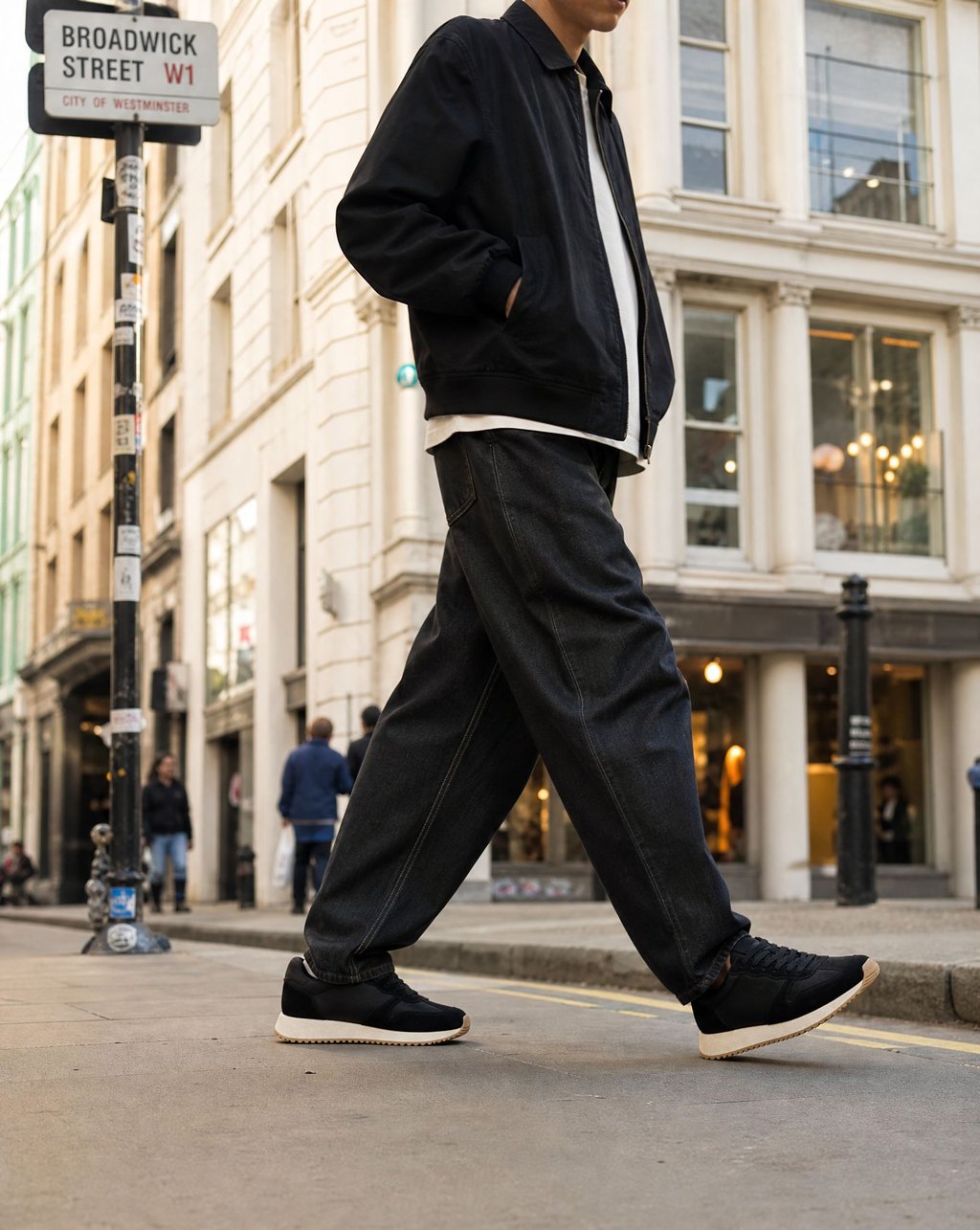 Black trainers with cream soles worn mid-stride on a Soho street in daylight