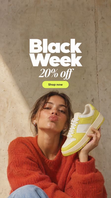 sneaker fashion product photo: A woman in a vivid rust-red sweater holds a white-and-lime sneaker against a sunlit concrete wall, with bold Black Week discount…