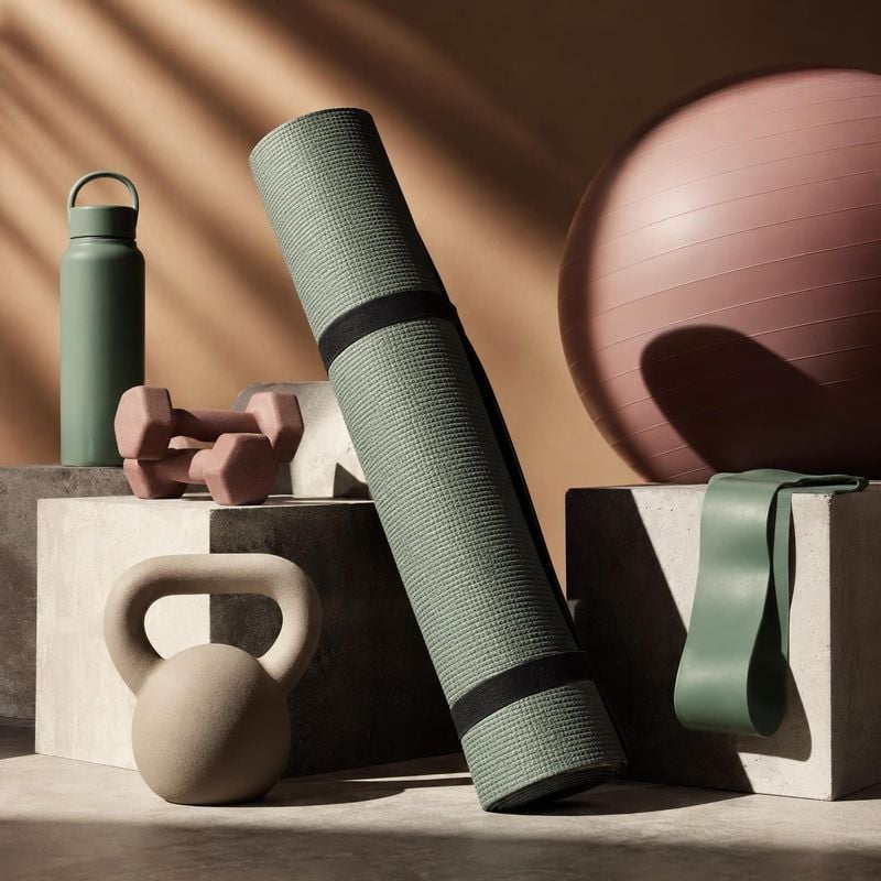 fitness equipment set group lineup product photo: A coordinated set of fitness gear—including a rolled yoga mat, weights, kettlebell, exercise ball, resistance…
