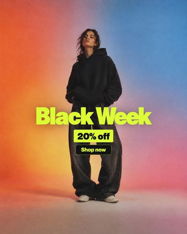 black hoodie and pants outfit fashion product photo: A model poses in an oversized black hoodie and loose pants against a softly lit orange-to-blue studio grad…