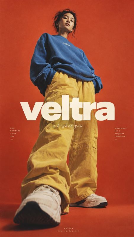 casual outfit look book product photo: A model poses in an oversized blue sweatshirt, loose yellow trousers, and sneakers against a vivid red studio backdrop,…