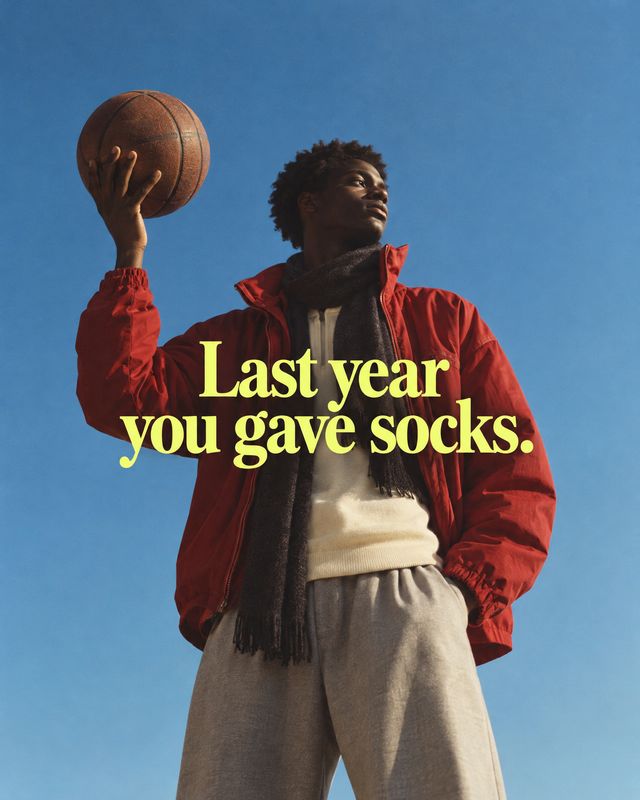 casual outfit look book product photo: A man in a red jacket, scarf and relaxed trousers holds a basketball against a clear blue sky, with bold yellow headline…