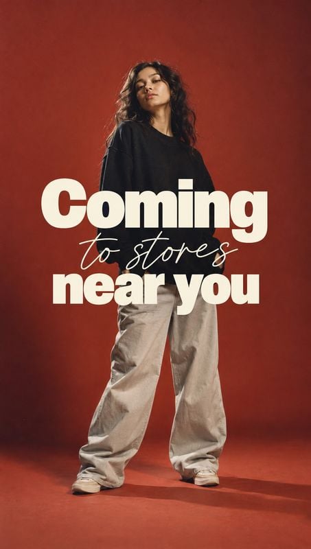 casual outfit look book product photo: A woman poses in a black top, loose light trousers and sneakers against a warm red studio backdrop, with bold cream lett…