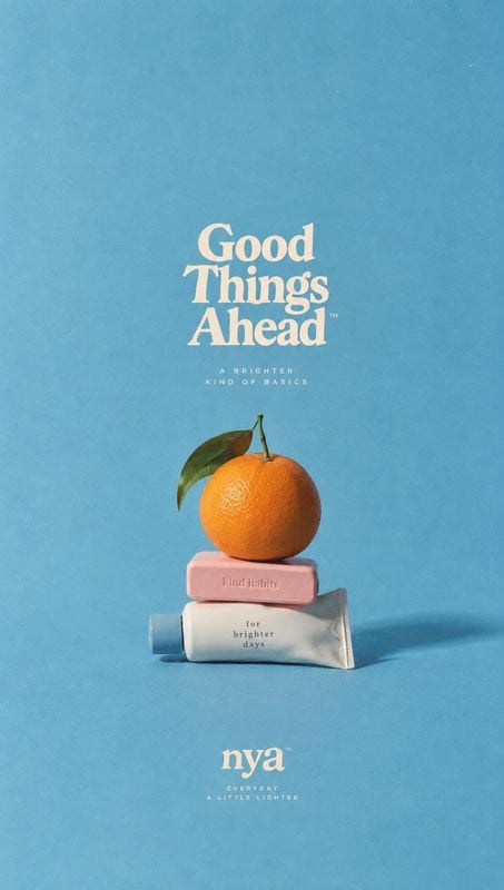 toothpaste tube and bar soap still life product photo: A toothpaste tube and pink soap bar are stacked beneath an orange on a seamless blue studio surface, wit…