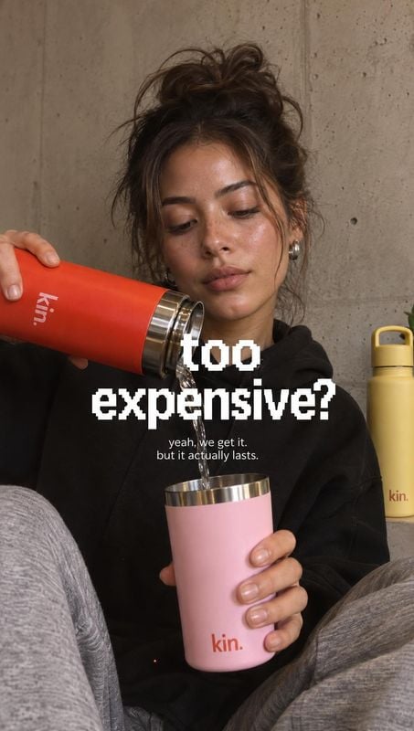 insulated tumbler lifestyle scene product photo: A woman in a black hoodie pours from a red insulated tumbler into a pink cup against a raw concrete wall, with…