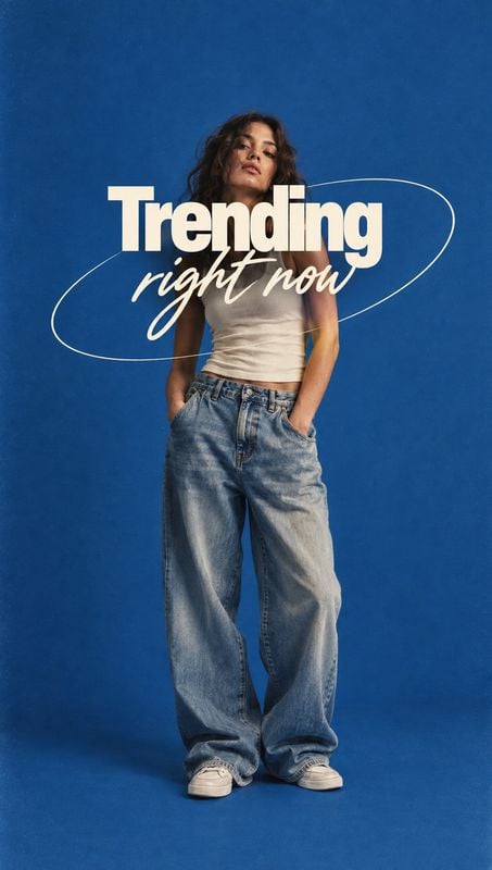 jeans look book product photo: A model poses in loose blue jeans, a white top and sneakers against a vivid blue studio backdrop, with bold cream lettering and…