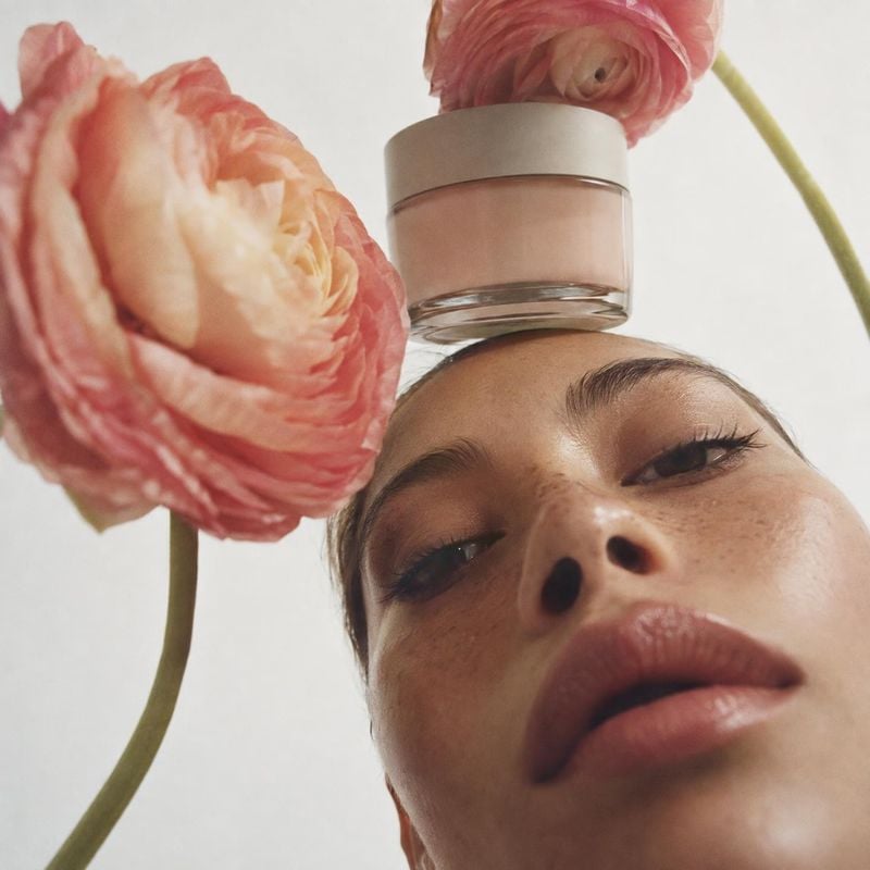 cosmetic cream jar beauty close-up product photo: A close-up beauty portrait places a simple cream jar above the model’s forehead, framed by pink flowers in so…