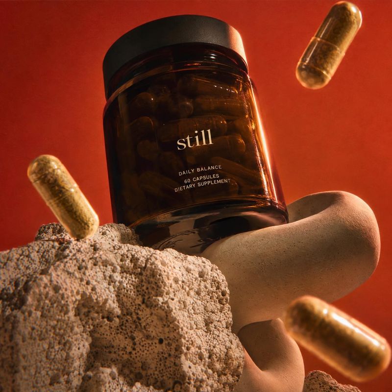 dietary supplement capsules personal care product photo: An amber supplement bottle and floating capsules are arranged among porous stone forms against a vivid…