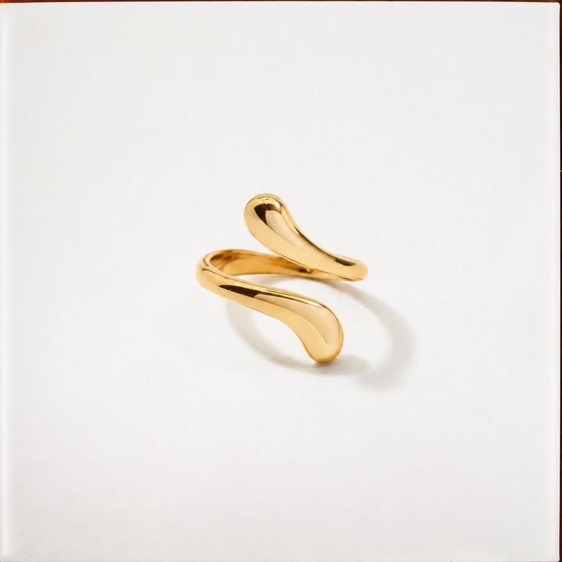 gold ring packshot product photo: A sculptural polished gold ring is isolated against a clean white surface, with soft studio lighting and generous open space…