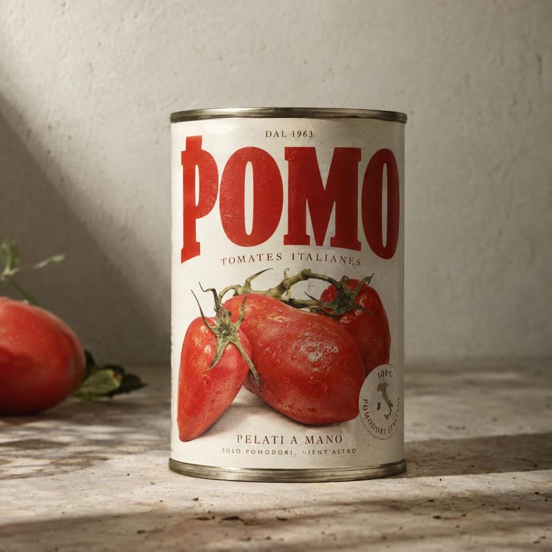 canned tomatoes food and drink product photo: A vintage-style can of Italian tomatoes stands on a sunlit stone surface beside a fresh tomato, creating a warm,…