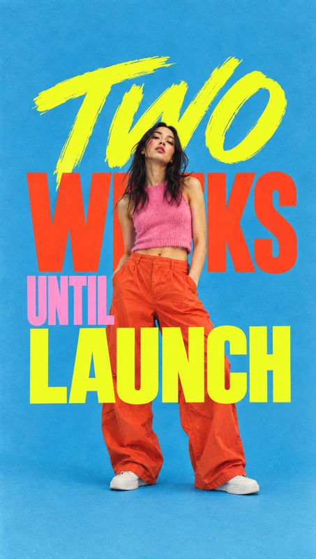 women’s outfit look book product photo: A model poses in a pink crop top and orange trousers against a bright blue studio backdrop, layered with bold yellow, r…