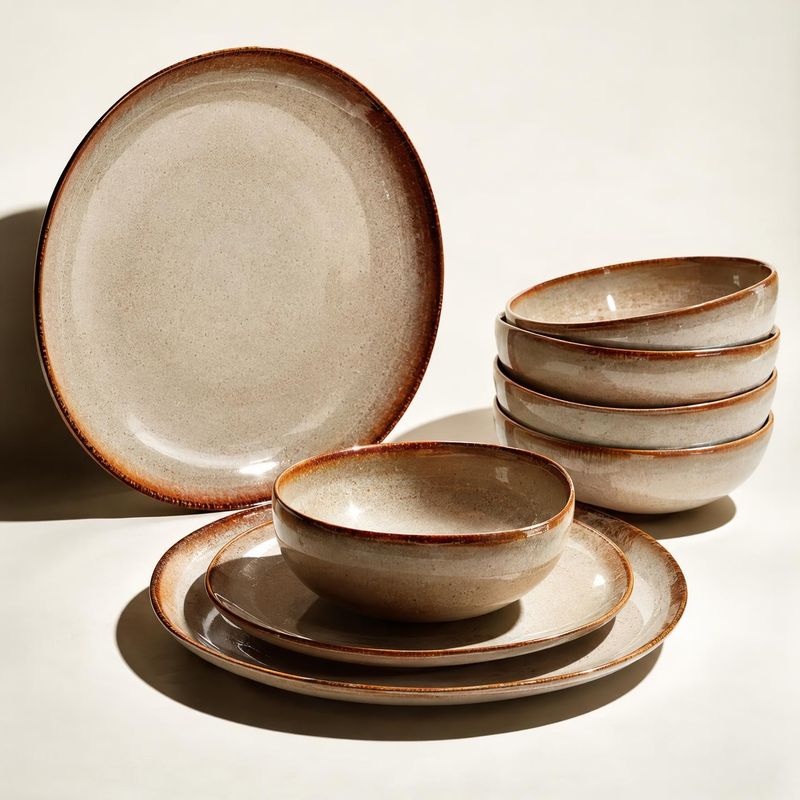 stoneware dinnerware set group lineup product photo: A coordinated set of cream-speckled stoneware plates and bowls with warm brown rims is arranged on a pale…