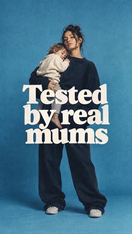 model try-on product photo: A mother in a dark casual outfit holds a young child against a textured blue studio backdrop, with oversized cream lettering and a…