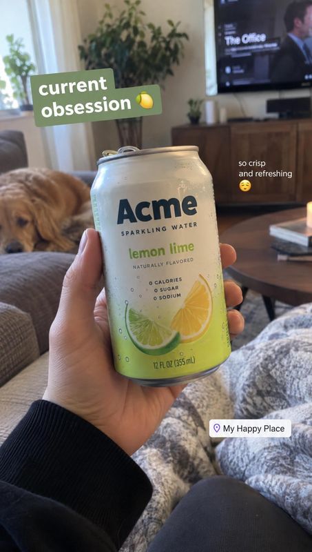 lemon-lime sparkling water product in hand product photo: A hand presents a lemon-lime sparkling water can in a cozy living room, with a dog resting nearby and…