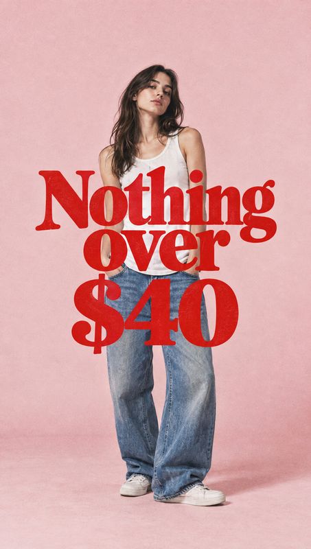 jeans model try-on product photo: A woman in a white tank top, loose blue jeans, and sneakers poses against a pink studio backdrop, with bold red “Nothing over…