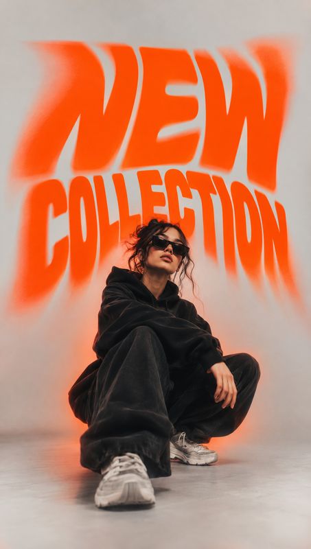 black streetwear outfit look book product photo: A model in an oversized black streetwear outfit and sunglasses poses low against a pale studio backdrop, frame…