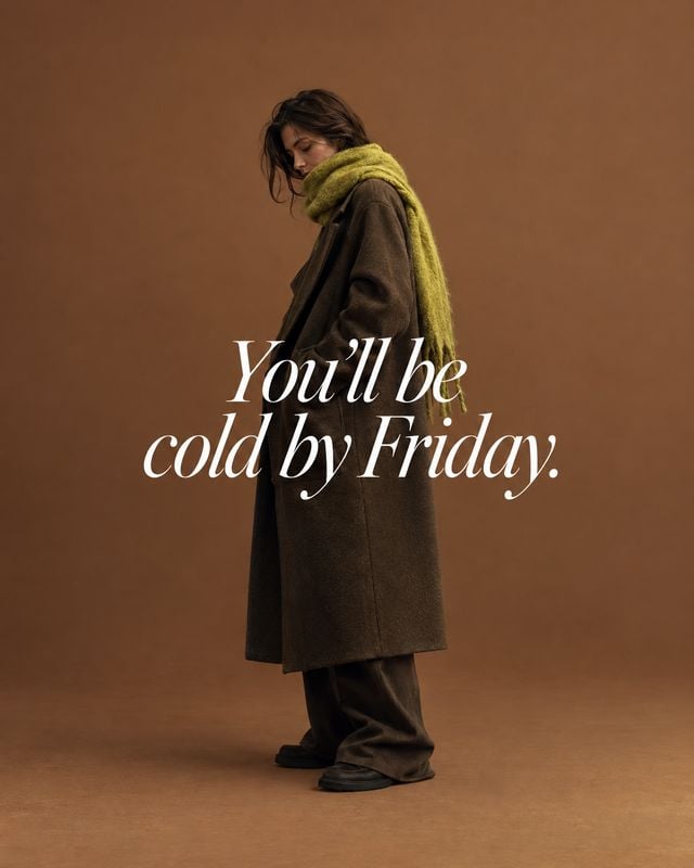 long wool coat and scarf autumn product photo: A model in a long dark coat and bright olive scarf stands against a warm brown studio backdrop beneath a large w…
