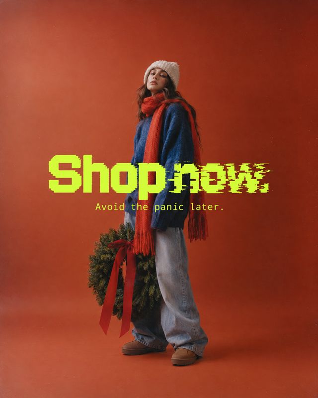 winter outfit model try-on product photo: A model in a blue sweater, red scarf, and loose jeans stands with a festive wreath against a warm red studio backdrop…
