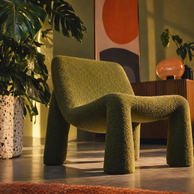 upholstered armchair room set product photo: A sculptural olive-green textured armchair anchors a plant-filled modern interior, lit with warm directional light…