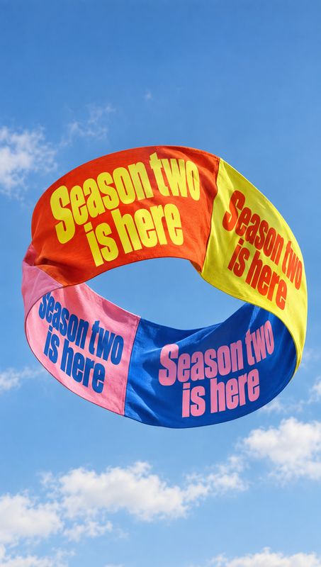 posters product photo: A colorful fabric ring printed with “Season two is here” floats against a bright blue sky, creating a lively, celebratory announcement.