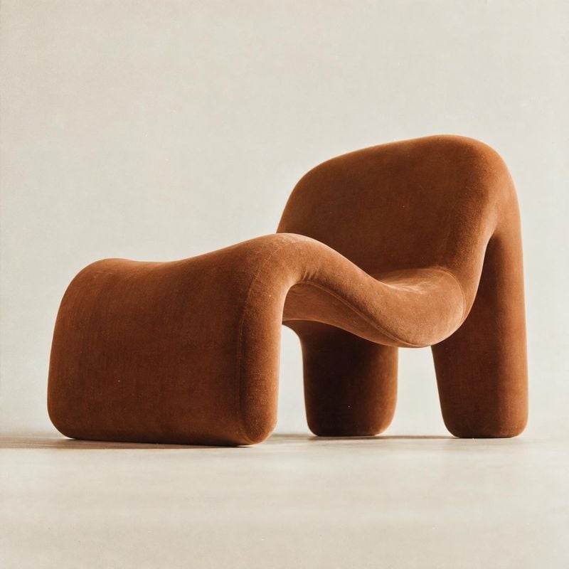upholstered lounge chair packshot product photo: A sculptural rust-brown upholstered chair sits alone against a warm off-white studio backdrop, with soft even…