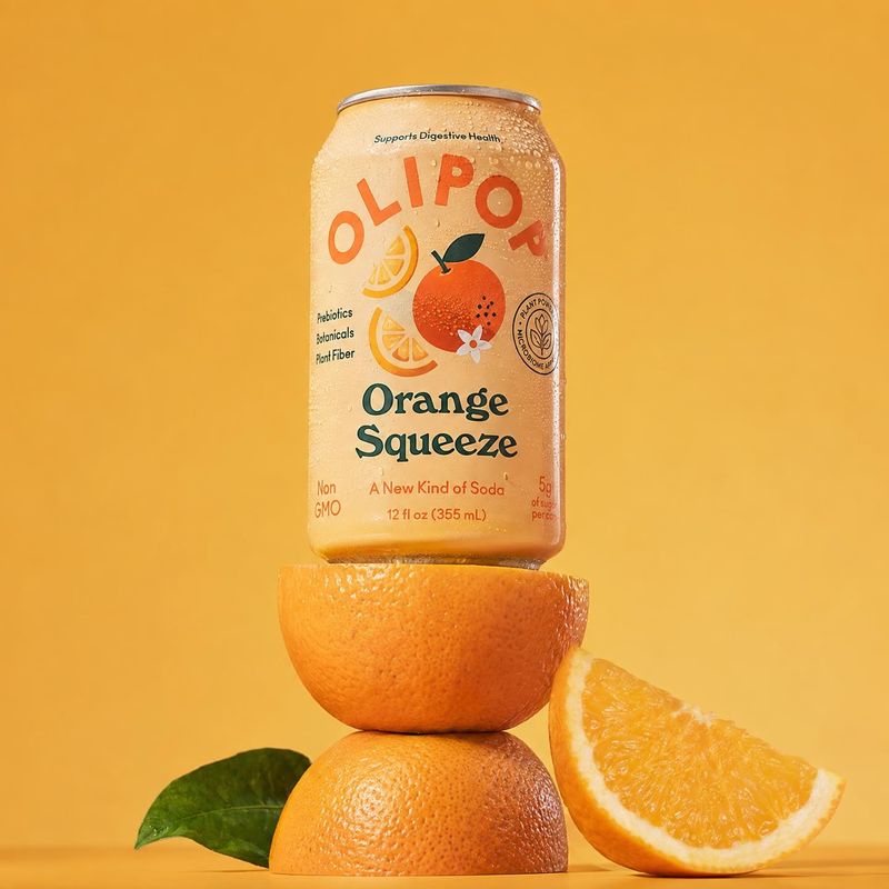 OLIPOP Orange Squeeze soda ingredients product photo: A chilled OLIPOP Orange Squeeze can is balanced on fresh oranges with a leafy sprig and orange wedge agai…