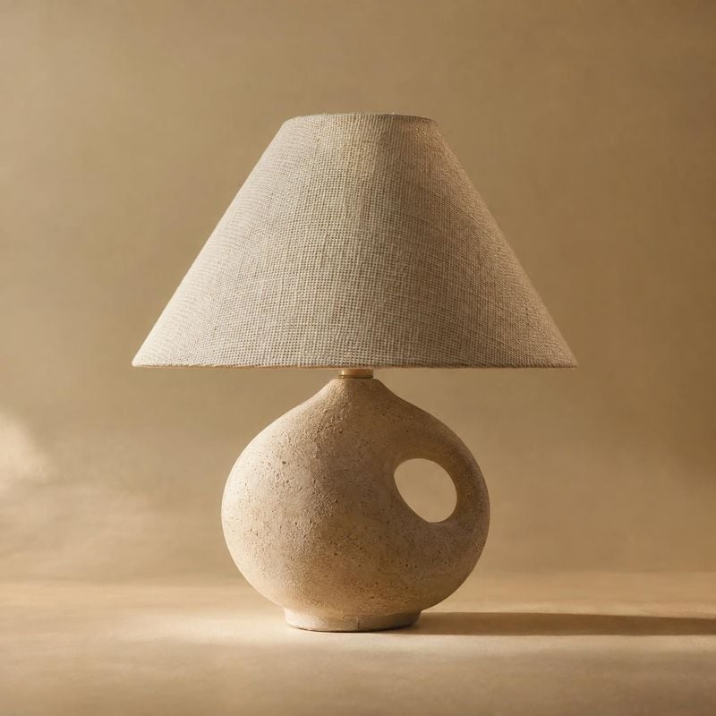 table lamp packshot product photo: A sculptural ceramic table lamp with a woven natural-fiber shade sits against a warm beige studio backdrop, lit with soft di…