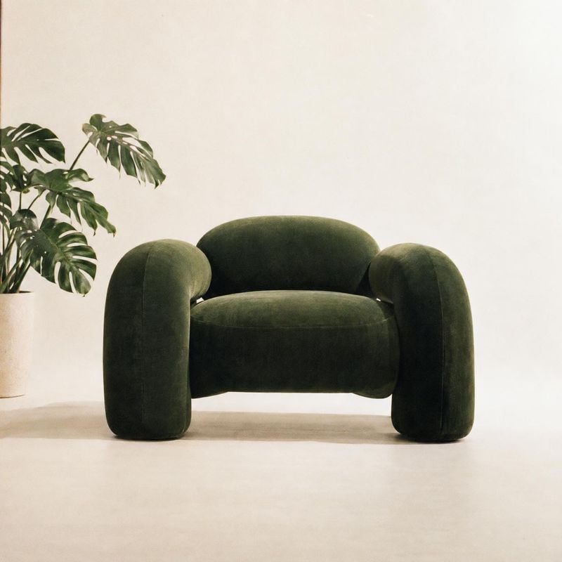 upholstered armchair room set product photo: A sculptural dark green upholstered armchair sits against a softly lit cream wall beside a leafy potted plant, cre…