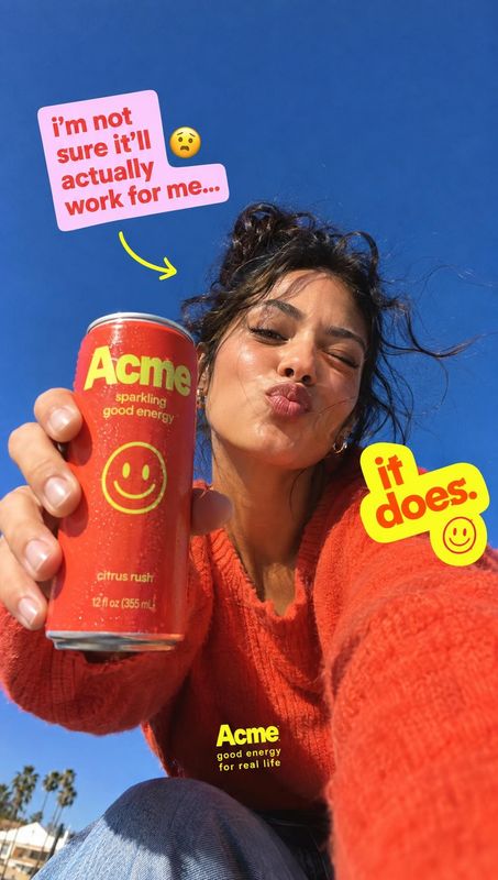 sparkling energy drink lifestyle scene product photo: A woman in a vivid orange sweater presents a red sparkling energy drink can against a bright blue sky, wi…