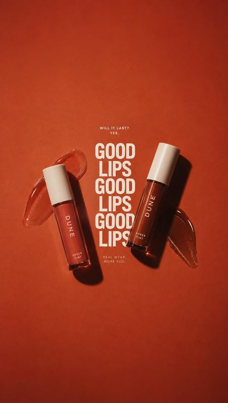 lip gloss still life product photo: Two DUNE lip gloss tubes are arranged diagonally with glossy swatches on a warm red backdrop, while bold cream typography a…