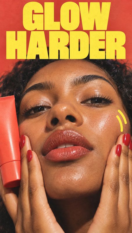 skincare tube beauty close-up product photo: A close-up beauty portrait shows a woman with glossy skin and red nails touching her face beside a red skincare tu…