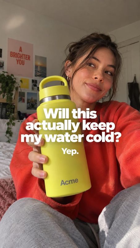 insulated water bottle lifestyle scene product photo: A woman in a red sweatshirt holds a bright yellow insulated bottle in a cozy room, while bold white headl…