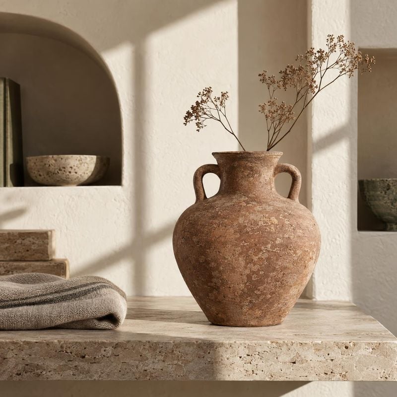 ceramic vase home product photo: A weathered terracotta vase with dried branches sits among natural stone and woven linen in a softly sunlit, neutral interior,…