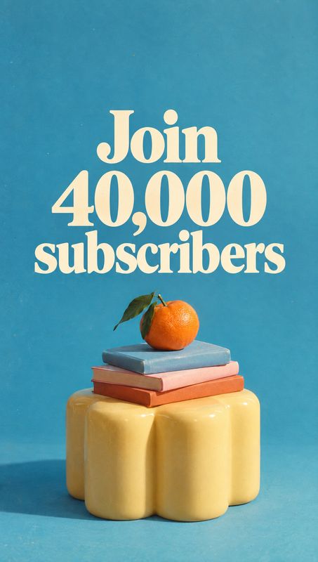 still life product photo: A bright orange rests on a stack of books atop a sculptural yellow pedestal against a turquoise studio backdrop, with large cream let…