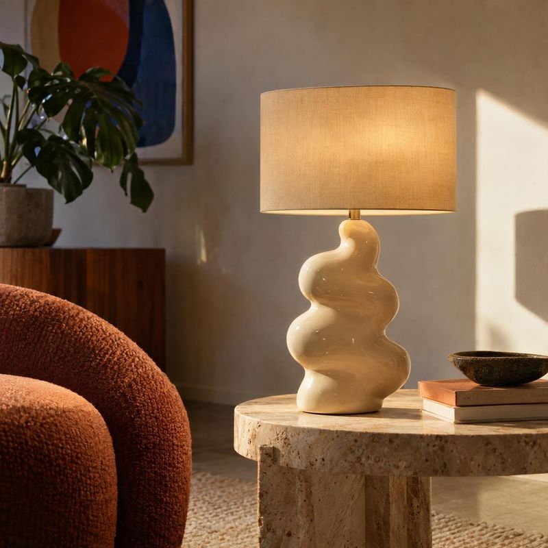table lamp room set product photo: A sculptural cream table lamp glows on a stone coffee table in a warm, sunlit living room, surrounded by textured seating, b…