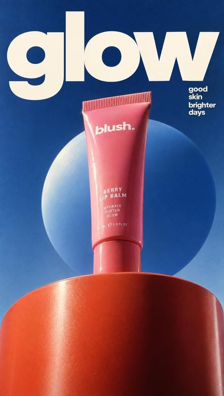 berry lip balm packshot product photo: A pink berry lip balm tube stands on a glossy red pedestal against a deep blue backdrop and glowing sphere, with oversiz…